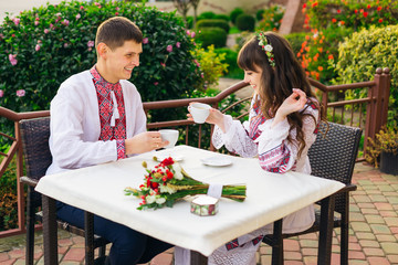 guy and girl in embroidered clothes sitting in cafe and drinking