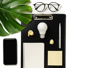 Financial planning table top with clipboard mockup, monstera leaves, pen, notebook, modern smartphone, eyeglasses and light bulb on white background minimal style. Concept brainstorming and new idea