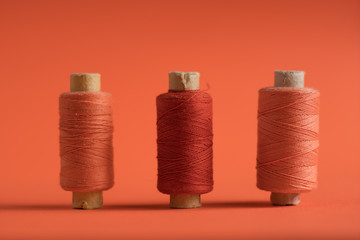 A coral spool of threads on coral paper background, with copy space.