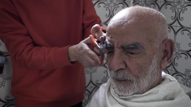 Very old Turkish Muslim Grandfather having his eyebrows trimmed by his grandson in his vintage bathroom designed in 1980's