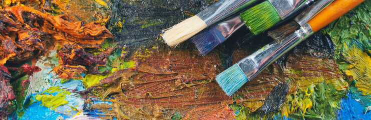 Closeup of art palette with colorful mixed paints and paintbrushed. Panorama. 