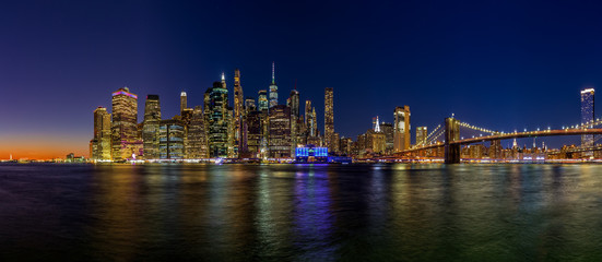Obraz na płótnie Canvas Panoramic image of lower Manhattan and the Brooklyn Bridge at night with the Hudson river reflecting the lights.
