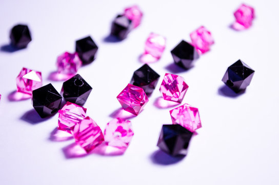 A scattering of beads on a white background, a sheet. Crystals. Iridescent and shiny pink and black beads. Materials for needlework. Style and fashion. For girls and children. Crystals close-up.