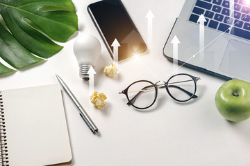 Modern workspace with light bulb, laptop, pen, monstera leaves, eyeglasses, fresh apple, smartphone and notebook with copy space on white background minimal style. Top view. Flat lay style.