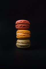 Stock photo of macarons of colors and flavors stacked in towers on black background.
