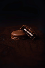 Stock photo of chololate cookies with one cut in half and showing a white filling on a black background.