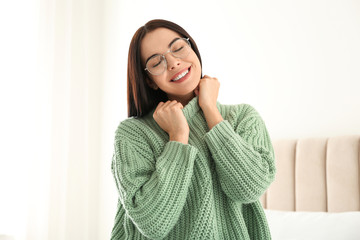 Young woman wearing warm sweater on bed at home. Winter season