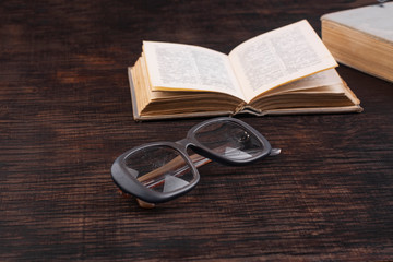 Old used glasses and book on a wooden table close-up.
