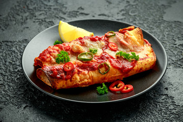 Baked Chicken fillets enchiladas with courgette, salsa sauce and cheese served with lemon wedges and chilies
