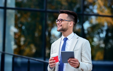 Businessman drinking coffee and using tablet in front of the corporation. Business, lifestyle concept