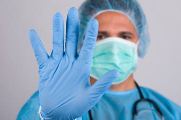 A young doctor in medical uniform with a protective face mask and a gloved hand showing a stop sign . Medical infects stopping concept.Stop COVID-19 concept.