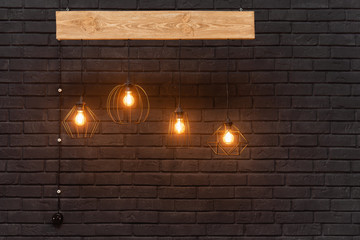 Orange retro lamps hanging on a wooden board on a background of dark black brick wall. Modern template with place for advertisement or text. Light Hanging Interior Design