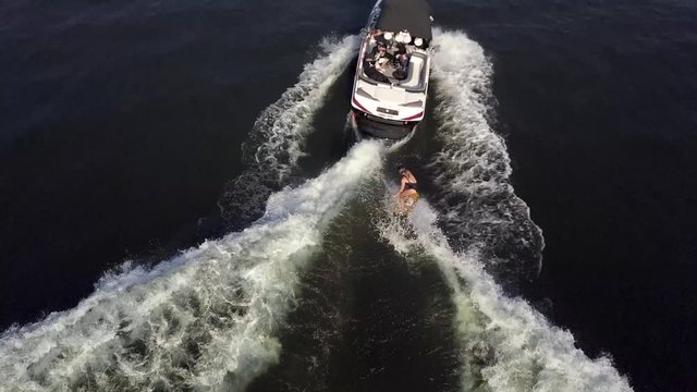Girl wake surfer riding a wave behind a boat. top view Dron.