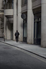 A person walks alongside a columnar building as he walks down the sidewalk on a lonely street