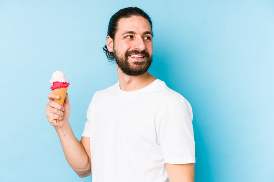 Young caucasian man eating an ice cream isolated looks aside smiling, cheerful and pleasant.