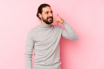 Young long hair man isolated on a pink background showing a mobile phone call gesture with fingers.