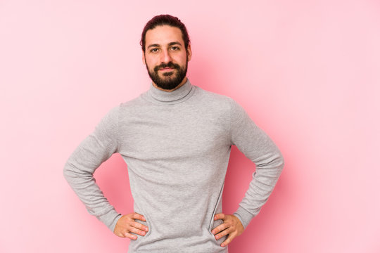 Young long hair man isolated on a pink background confident keeping hands on hips.