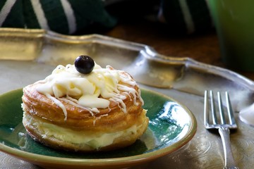 Custard pie with blue berries.  A custard filled pastry with icing on the top and decorated with a blue berrie.  The pastry sits on a green plate which is on a metal tray.  