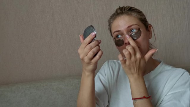 a young beautiful girl with black eye patches. morning treatments for skin in the mirror