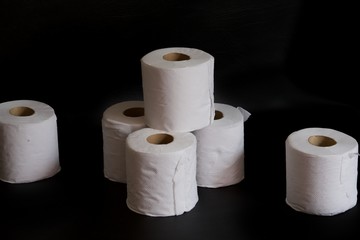 Multiple toilet paper rolls against a black background.  A stack of white tissue rolls contrasted against a dark background