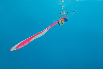 Russia, Samara - February 16, 2020 year. Сolgate pink toothbrush drops in an aquarium with water on a blue background