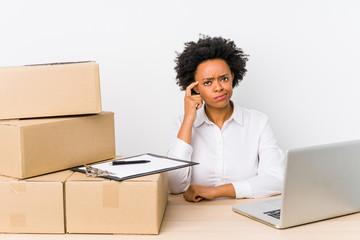 Warehouse manager sitting checking deliveries with laptop pointing temple with finger, thinking,...