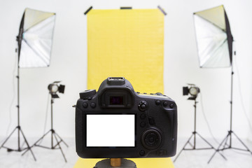 Camera in a photo studio with yellow backdrop and light equipment. White screen mockup