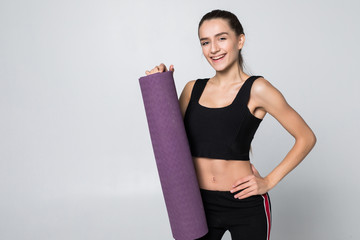Attractive woman in gym attire holding a mat in her outstretched arms isolated on white background