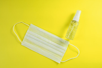 White face mask and alcohol gel on yellow background. Surgical mask and antibacterial soap sanitizer