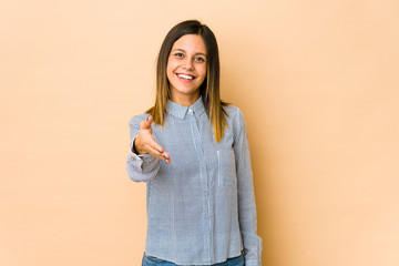 Young woman isolated on beige background stretching hand at camera in greeting gesture.