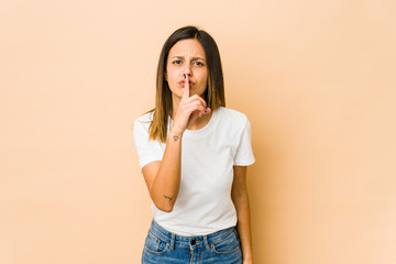 Young woman isolated on beige background keeping a secret or asking for silence.