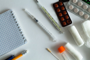 medical thermometer and pills for the treatment of disease on a white background. medicines, injection ampoules, bandages and syringes with pen and note book on a white table. health. top view