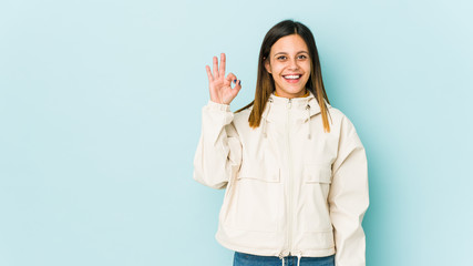 Young woman isolated on blue background cheerful and confident showing ok gesture.