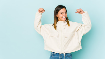 Young woman isolated on blue background showing strength gesture with arms, symbol of feminine power