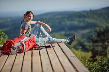 young female sitting on viewpoint high in mountain, looking at camera. nature, relaxing, filling with energy concept