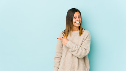 Young woman isolated on blue background smiling and pointing aside, showing something at blank space.