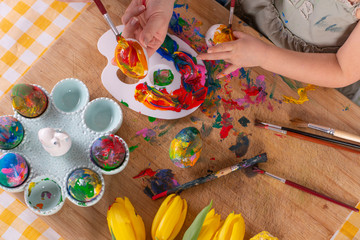 Little hands of girl decorate and paint easter eggs in different color on a wooden table....