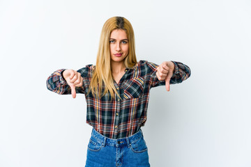 Young blonde woman isolated on white background showing a dislike gesture, thumbs down....