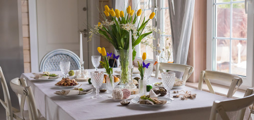 Easter festive spring table setting decoration, eggs in nest, fresh yellow tulips, marshmallows, selective focus banner