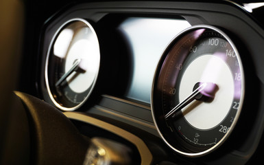 Instrument cluster of a modern luxury car. In the foreground, the speedometer is in focus, in the background the tachometer and multifunction display are blurred.