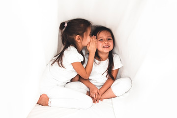 Cute little girl whispering something to her sister under the cover