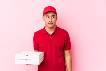 Young pizza delivery latin man isolated confused, feels doubtful and unsure.