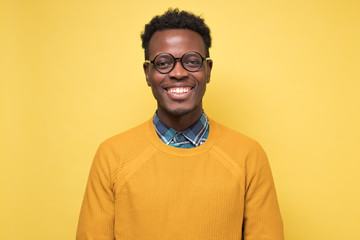 Young handsome african business man in glasses posing isolated over yellow wall.