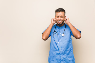 Young south-asian nurse man covering ears with hands.
