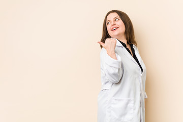 Young doctor woman points with thumb finger away, laughing and carefree.