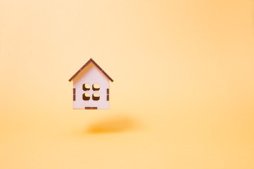 Fototapeta na wymiar a small wooden decorative house flies on a yellow background, the levitation of the item, the place of the copy, the sale and construction of houses concept