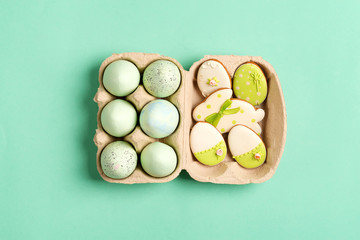 Easter composition from craft painted eggs in paper box and baked cookies on a green background.