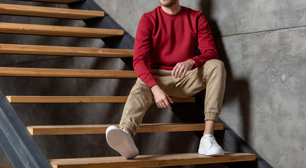 Man at home in burgundy blank sweatshirt or long sleeved. Sitting on the stairs near the wall at...