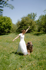 A young girl in a white dress is in the park with her pet dog briard.Spring time.