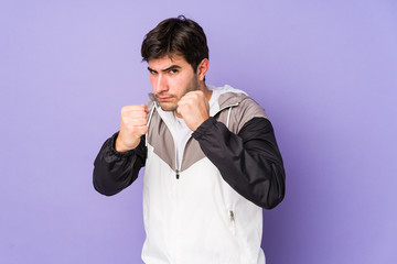 Young man isolated on purple background showing fist to camera, aggressive facial expression.